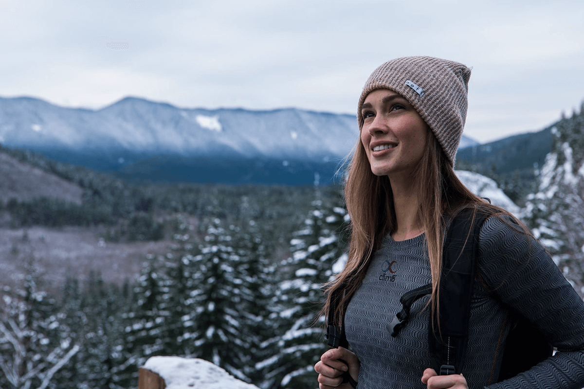 A woman stands on top of a snow covered mountain wearing a hat and smart shirt